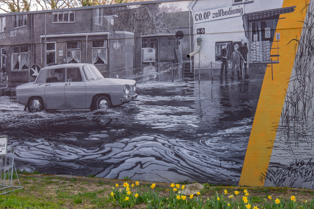 Paul Wieggers heeft met zijn muurschildering de historie van deze plek zichtbaar willen maken. De thema's water en landschap komen terug in het ontwerp. Het linkse fragment heeft een foto uit 1966 als onderwerp met de watermassa bij de Driehoek na een hevige regenbui. Zichtbaar is nog de COOP-winkel die inmiddels is gesloopt. 
Het rechtse onderwerp betreft een fragment van een een doorwaadbare plaats in een rivier of moeras noemen we ook wel een 'voorde'. Zo zijn diverse plaatsnamen ontstaan met het woord 'voorde' er in. Zoals Bredevoort, Amersfoort, het Duitse Erfurt, het Engelse Oxford en natuurlijk Lichtenvoorde.