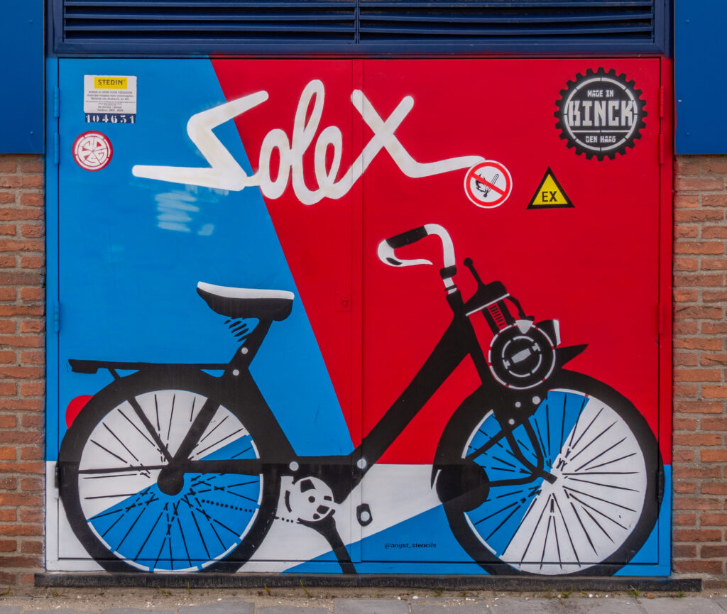 Een gestencilde affiche van een solex, die in Binckhorst werden gemaakt staat op een electriciteitshuisje bij een bedrijfsverzamelgebouw. Ook zijn stempelontwerp 'Mede in de Binckhorst'staat rechtsboven