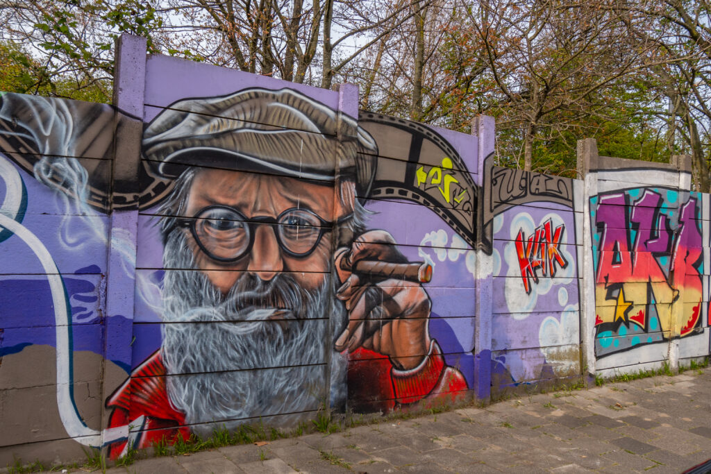 De hele 100 meter lange muur is één grote Akbar Tribute. Als straatfotograaf is Akbar Simonse wereldberoemd in de Haagse Street Art scene. Hij fotografeert alle graffiti en Street Art die er in de stad gemaakt wordt. Maar Akbar is ongeneeslijk ziek en daarom wilden de Street Art artiesten uit Den Haag en omstreken hem een hart onder de riem steken. Het is één groot(s) eerbetoon aan Akbar.