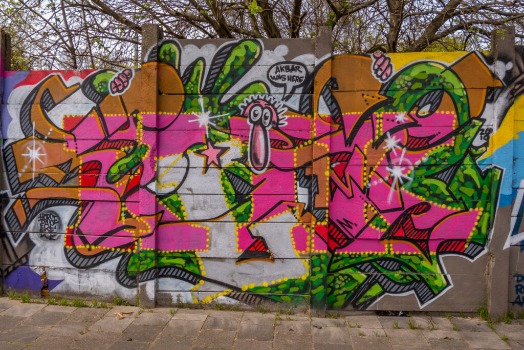 De hele 100 meter lange muur is één grote Akbar Tribute. Als straatfotograaf is Akbar Simonse wereldberoemd in de Haagse Street Art scene. Hij fotografeert alle graffiti en Street Art die er in de stad gemaakt wordt. Maar Akbar is ongeneeslijk ziek en daarom wilden de Street Art artiesten uit Den Haag en omstreken hem een hart onder de riem steken. Het is één groot(s) eerbetoon aan Akbar.