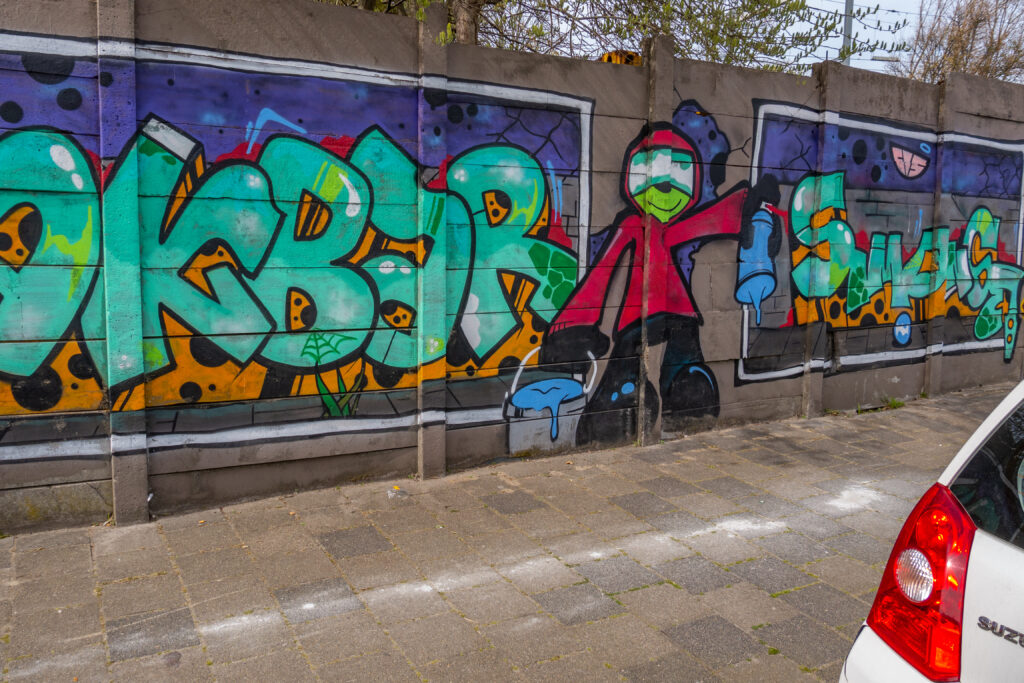 De hele 100 meter lange muur is één grote Akbar Tribute. Als straatfotograaf is Akbar Simonse wereldberoemd in de Haagse Street Art scene. Hij fotografeert alle graffiti en Street Art die er in de stad gemaakt wordt. Maar Akbar is ongeneeslijk ziek en daarom wilden de Street Art artiesten uit Den Haag en omstreken hem een hart onder de riem steken. Het is één groot(s) eerbetoon aan Akbar.