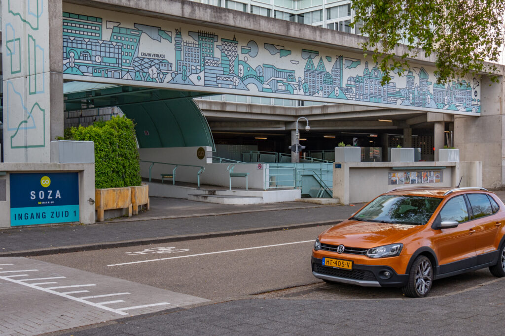 Aan het begin van de zomer hadden we all een mooie mural i.s.m. statushouders op de achterzijde van het pand gemaakt en nu was het beurt aan Erwin Verkade om zijn visie van het "Central Innovation District" op de voorzijde af te beelden.

Op de poort van SoZa is nu de CID skyline te zien met de stations CS, HS en Laan van NOI, “Het Strijkijzer”, “De Netkous” (de trambaan op de Prinses Beatrixlaan), de ministeries BZK en justitie aan de Turfmarkt en winkelcentrum New Babylon. Door middel van stemmen is Erwins ontwerp uitgekozen en eind augustus werd de mural officiëel onthuld door de wethouder van Mobiliteit, Cultuur en Strategie Robert van Asten.