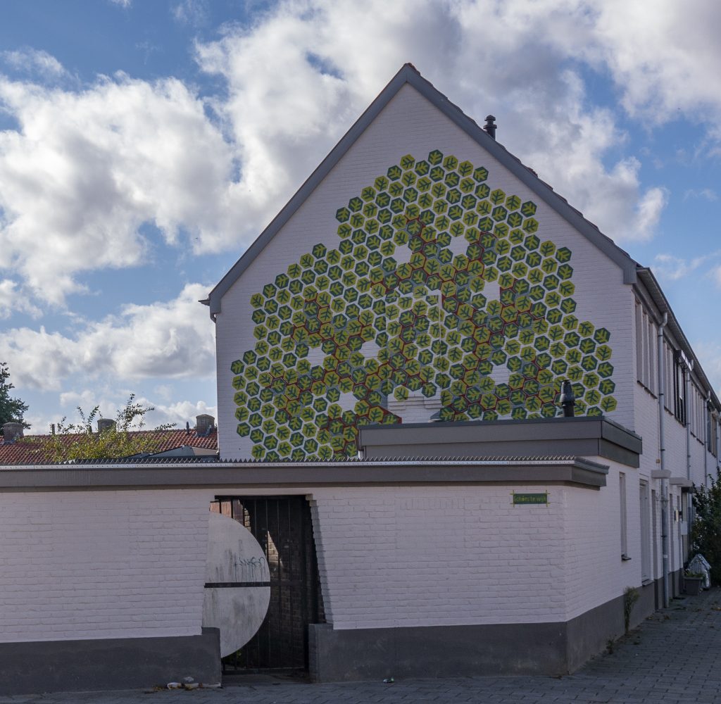 een enorme boom de gevel van een hoekhuis.1 De blaadjes staan symbool voor groei en het komen en gaan van bewoners in en uit de wijk.