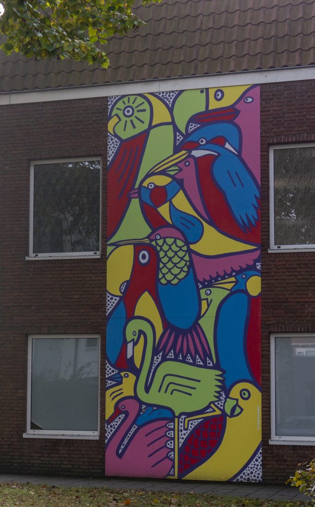 Muurschildering op de basisschool Koningshaven. Tijdens een workshop konden leerlingen van de school meehelpen aan deze 6,5 meter hoge muurschildering. Uitgangspunt voor het ontwerp van de muurschildering was het samenzijn en samenwerken op school en het multiculturele karakter van de school. De diverse kleurrijke vogels symboliseren de diversiteit van de school.