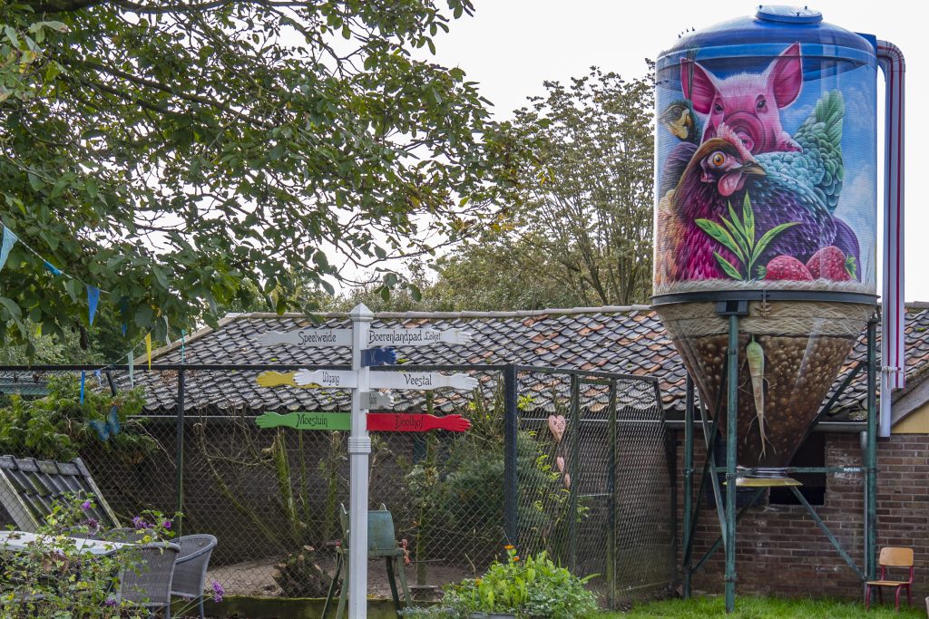 De wereld bekeken door de ogen van een kind: speels en kleurrijk. Het resultaat is een vrolijke beestenboel, waaronder het lievelingsdier van de eigenaren: de pauw. De aarde en de wortel in de trechter staan symbool voor o.a. de gewassen, de groei en de kringlooplandbouw. Alle onderdelen van het ontwerp zijn opgenomen in een ‘glazen melkfles’. Deze ‘melkfles’ heeft een vergelijkbare functie: het staat symbool voor een zelfvoorzienende wereld.