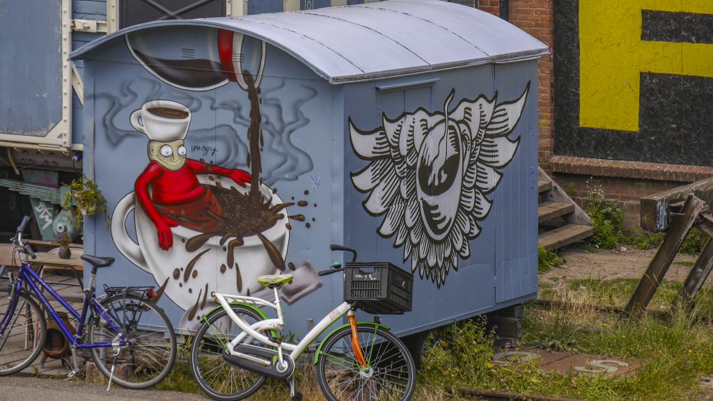 een oude treinwagon die nu dienst doet als koffiezaakje genaamd Stoom013. Je ziet een mannetje in een kop koffie die ook nog eens een kop koffie op zijn hoofd heeft.