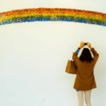 Regenbogenbrücke Eine Frau steht vor einer Mauer und sprüht einen Regenbogen darauf.