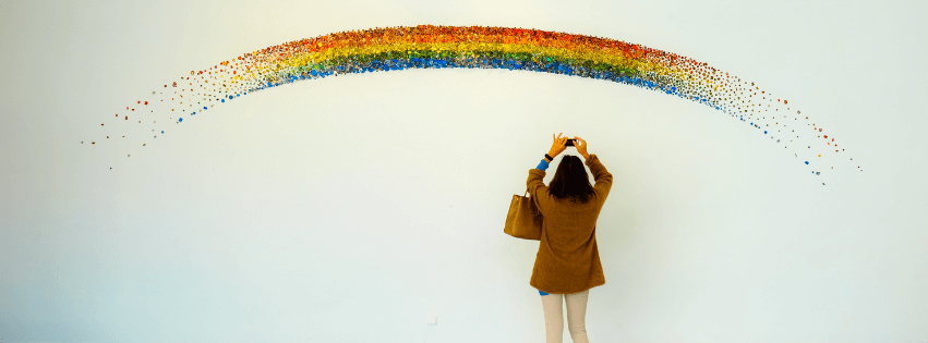 Regenbogenbrücke Eine Frau steht vor einer Mauer und sprüht einen Regenbogen darauf.