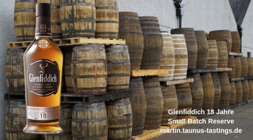Eine Flasche Glenfiddich 18 Jahre, im Hintergrund ein Lager mit leeren Whiskyfässern