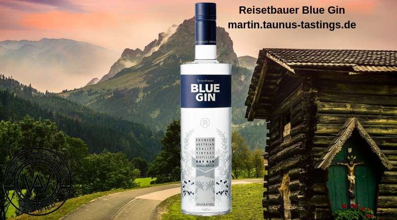 Eine Flasche Reisetbauer Blue Gin, im Hintergrund ein altes Holzhaus in Österreich