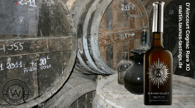 Eine Flasche D'Aincourt Cognac Rare XO mit alten Fässern im Hintergrund