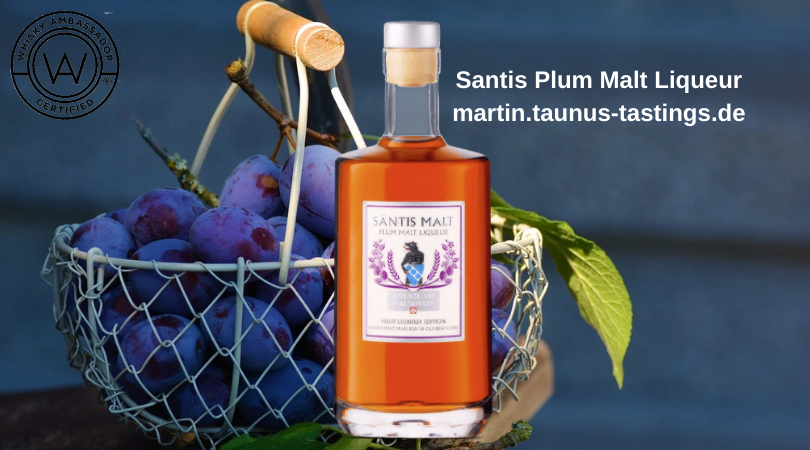 Eine Flasche Santis Plum Malt Liqueur mit einem Korb Pflaumen im Hintergrund