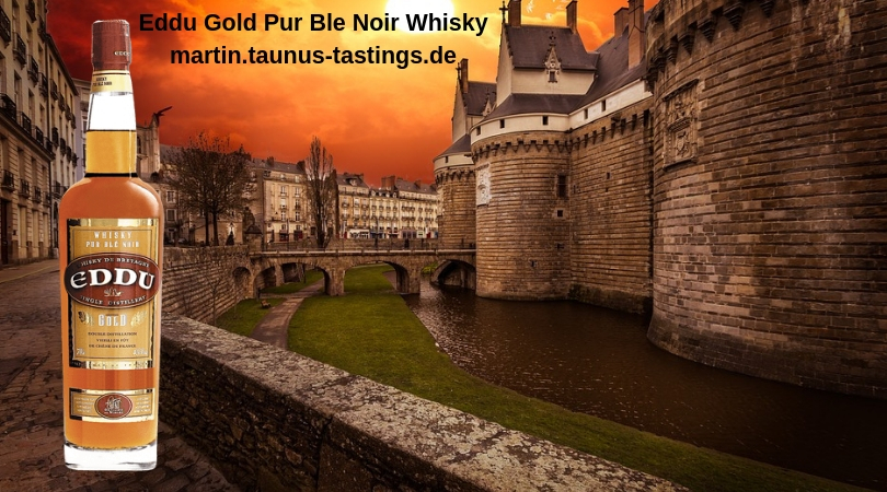 Eine Flasche Eddu Gold Pur Ble Noir Whisky, im Hintergrund Gebäude in der Bretagne