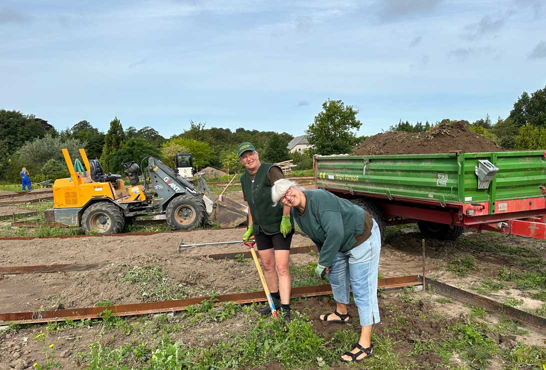 29. august 2023: Mette og Lissi fjerner tidsler i den nye have, Haven for de fem sanser, samtidig med, at en medarbejder fra haveanlægsfirmaet Stougaard etablerer metalkanter rundt om de kommende bede. 
