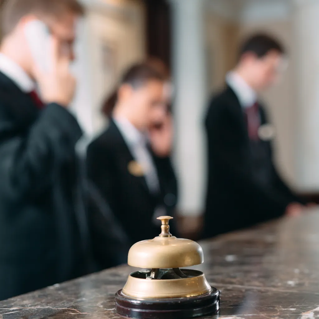 Brass service bell on a marble luxury hotel reception desk, with hotel staff working in the blurred background