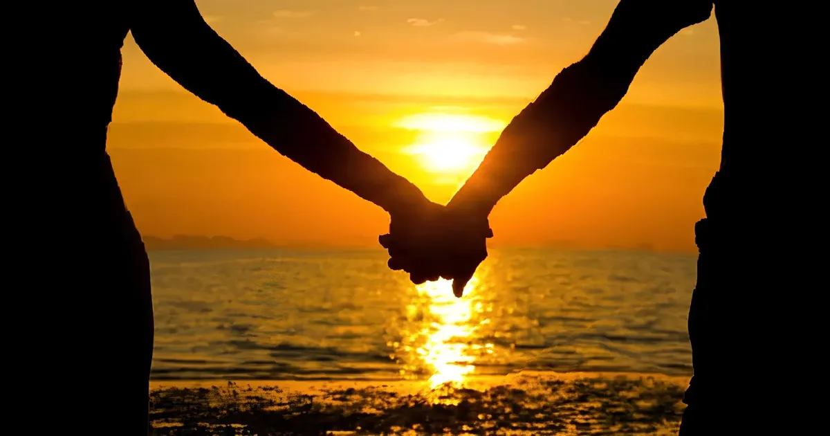 Silhouetted couple holding hands at golden sunset over ocean