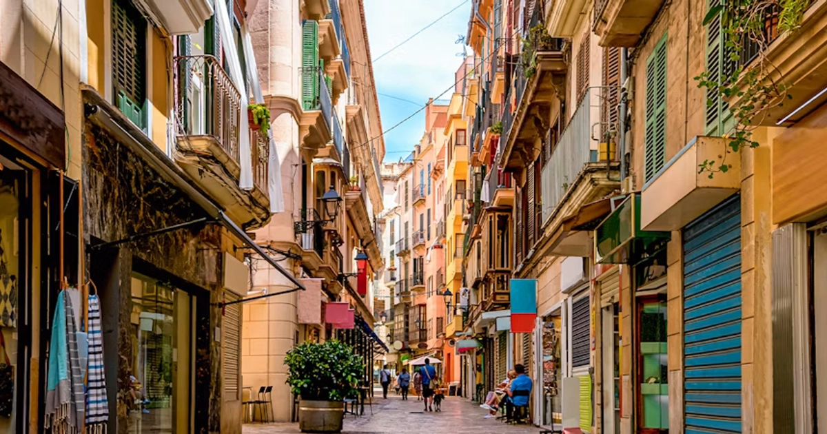 Narrow sunny street in Palma de Mallorca centre lined with colorful historic buildings and shoppers