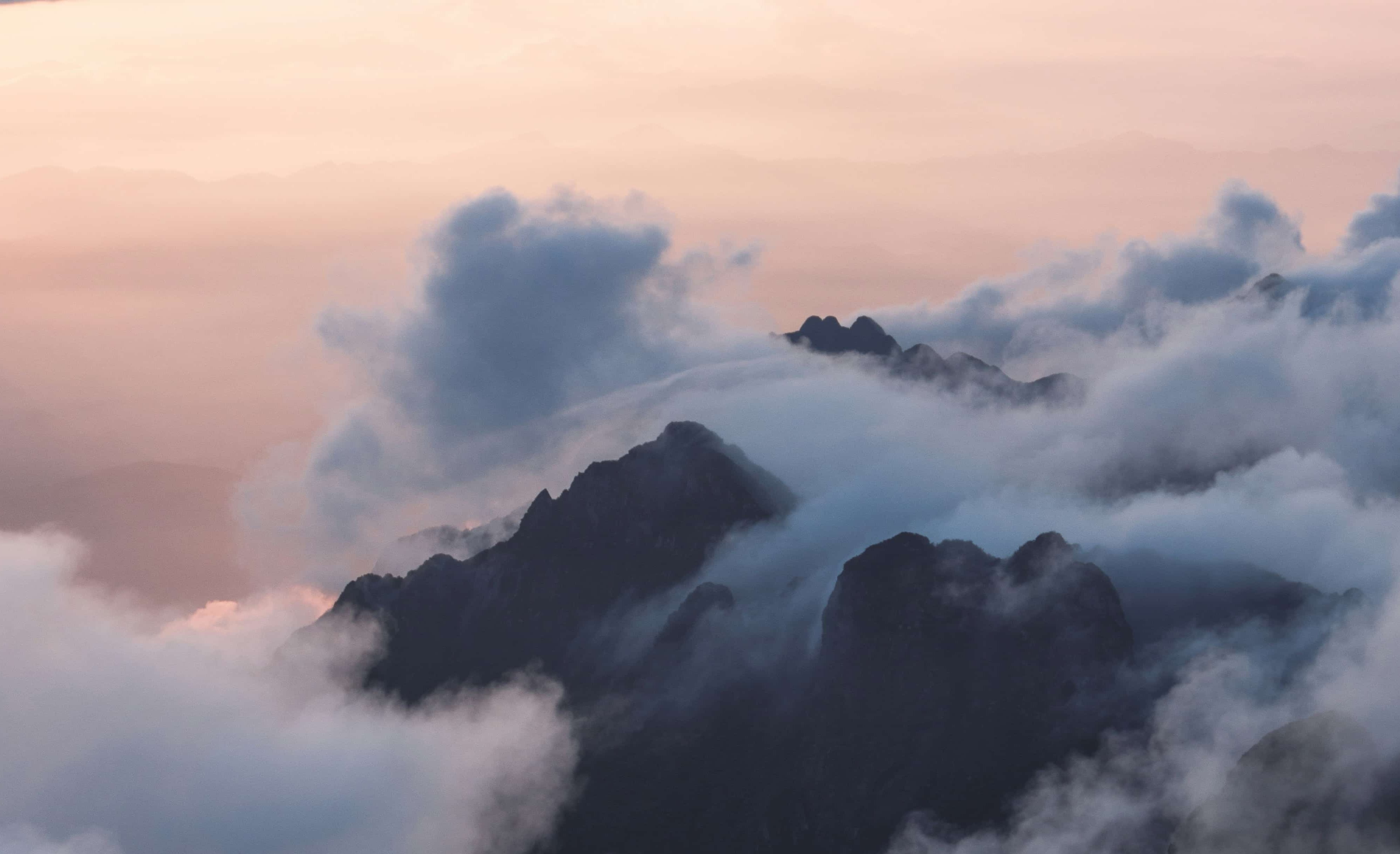 A photo of mountain covered in clouds. The sky is pink, and it is almost dark outside.