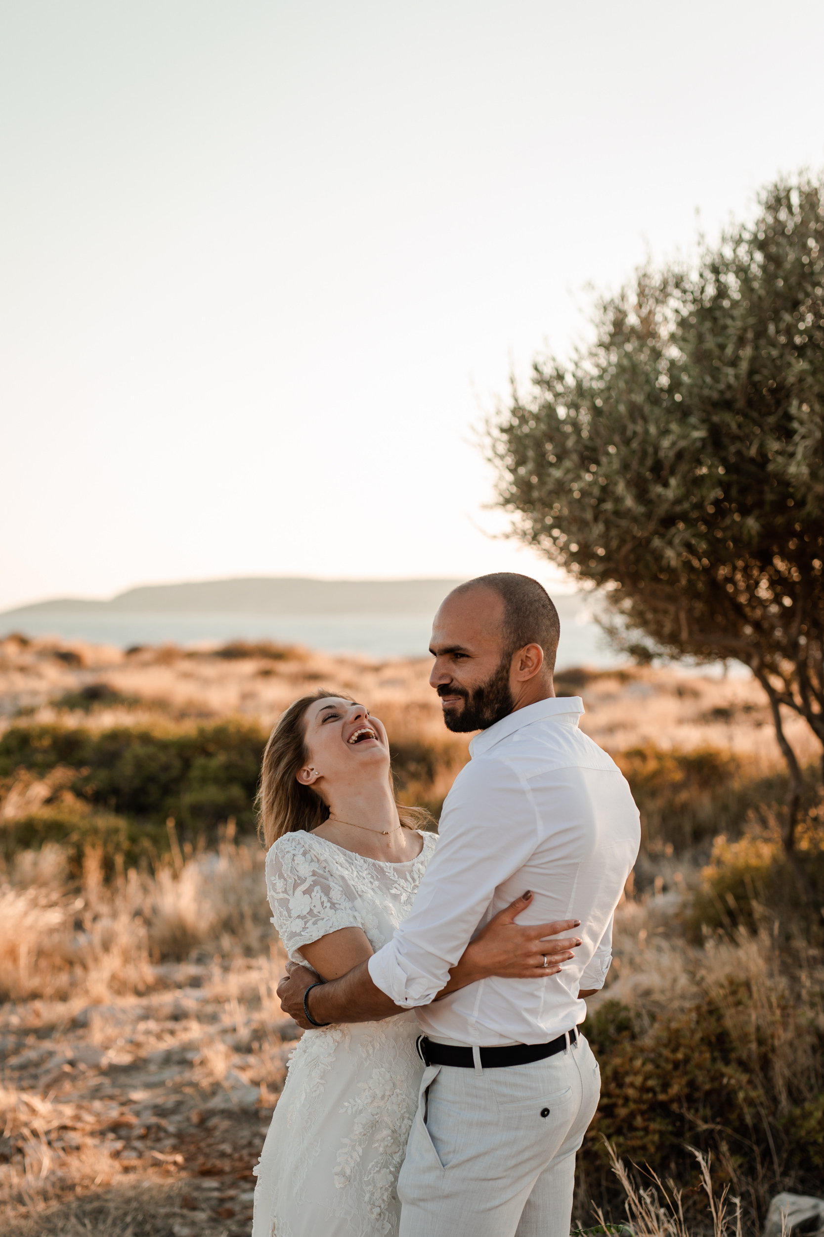 Bröllopspar skrattar under sin porträttsession i Grekland i solnedgången