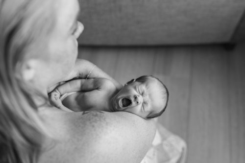 Bebis gäspar i sin mammas famn under en nyföddfotografering i Småland