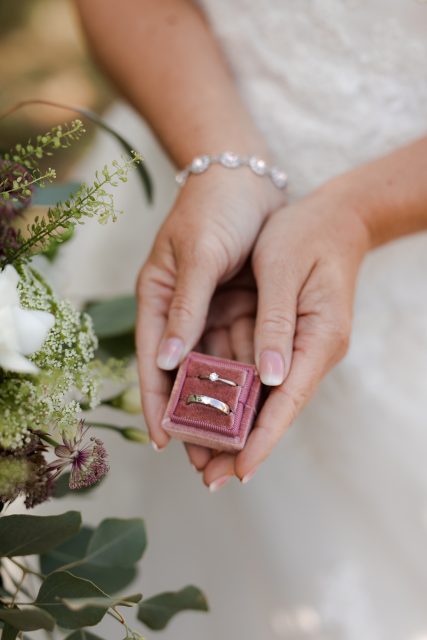 En bruds händer håller en rosa ringask i sammet med vigselringar