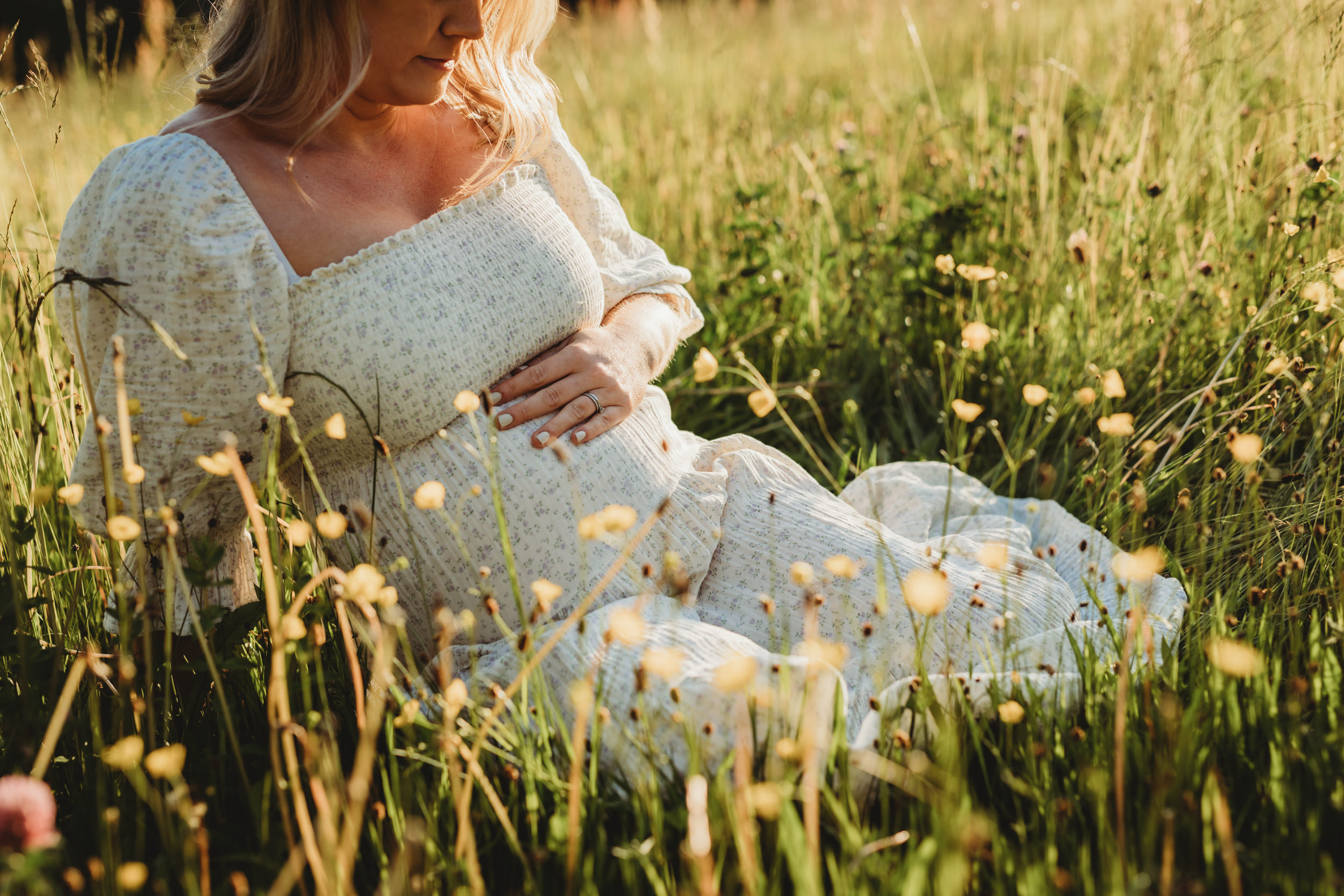Gravid kvinna sitter på en äng under en gravidfotografering