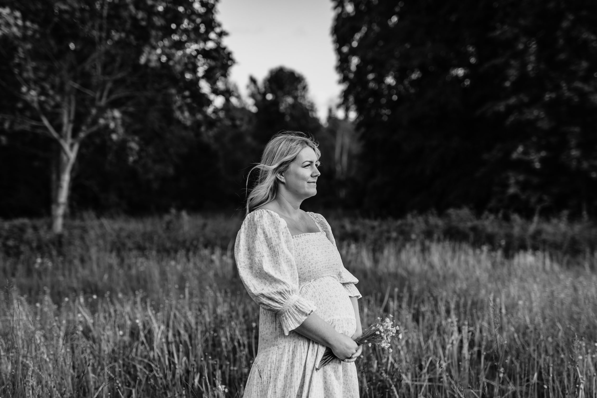 Gravid kvinna står på en blomsteräng under en gravidfotografering i Småland