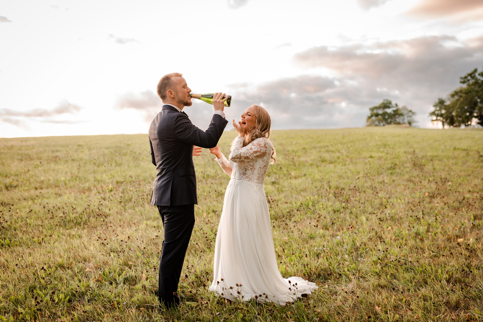 Bröllopsfotografering i Eksjö med brudpar på en äng som dricker champagne