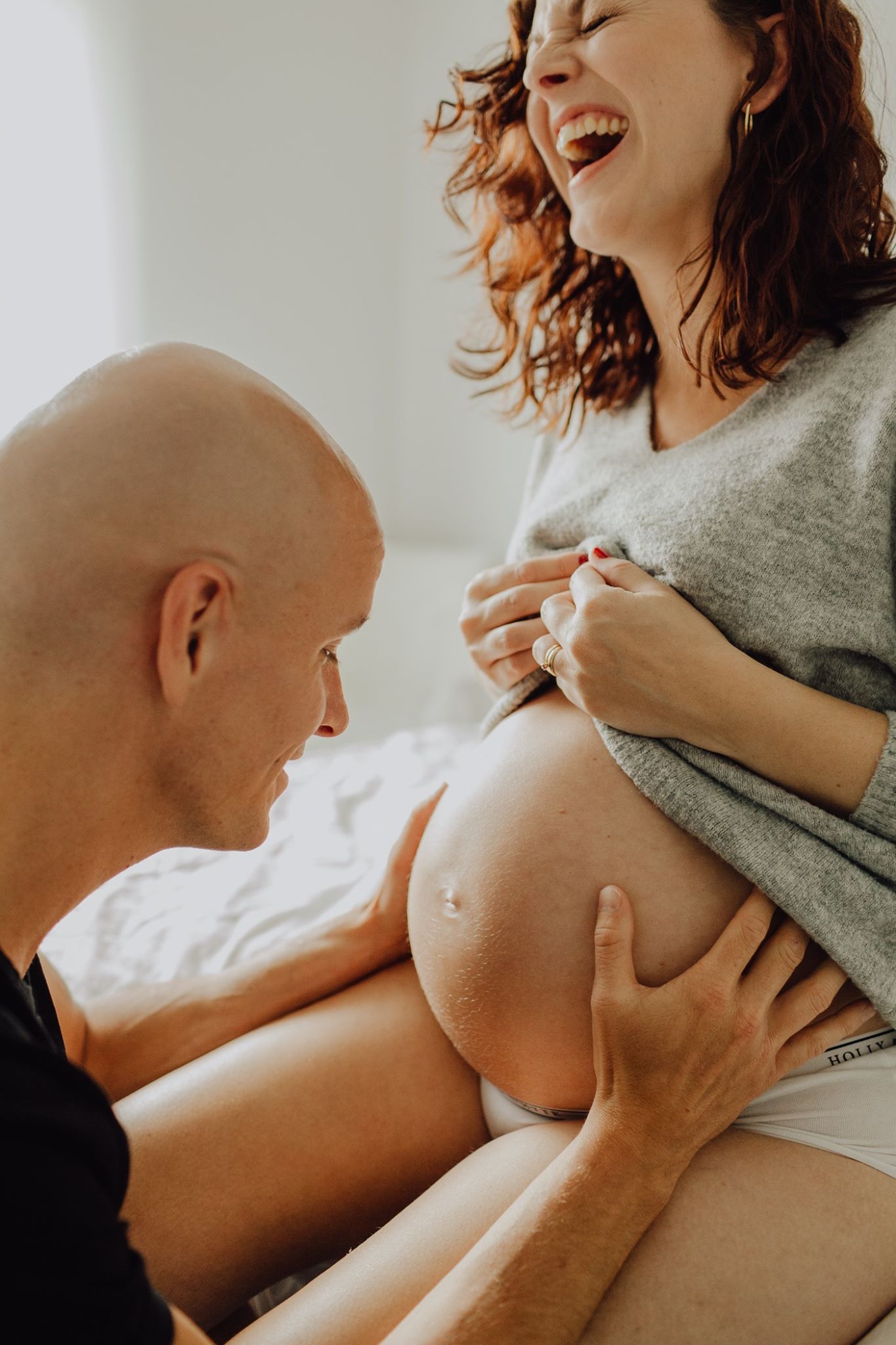 En blivande pappa håller om den gravida magen på sin fru som skrattar stort