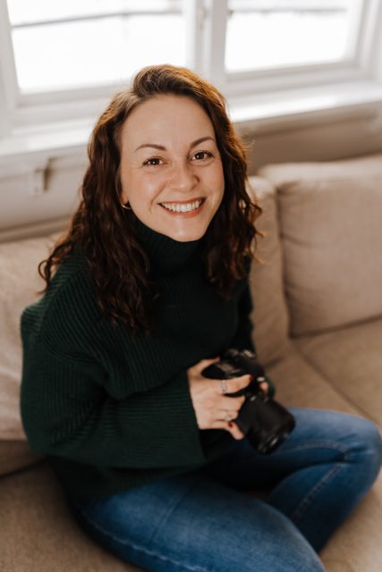 Mörkhårig glad kvinna sitter i soffan med en kamera i handen