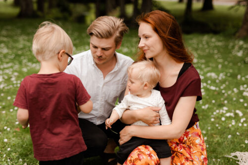 En pappa, mamma och två barn sitter på gräset på sin familjefotografering i Småland