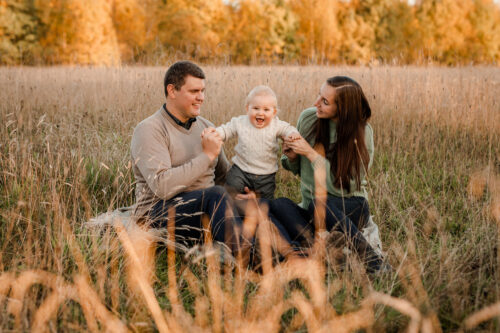 En mamma och en pappa busar med sin ettåriga son på ett fält i solnedgången på en familjefotografering i Småland