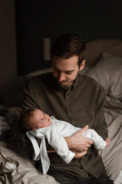 En nybliven pappa håller sin nyfödda bebis i famnen under en nyföddfotografering i Småland