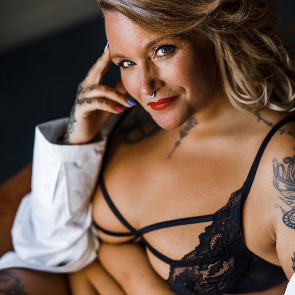 Plus size kvinna i svarta underkläder och vit skjorta på en boudoirfotografering