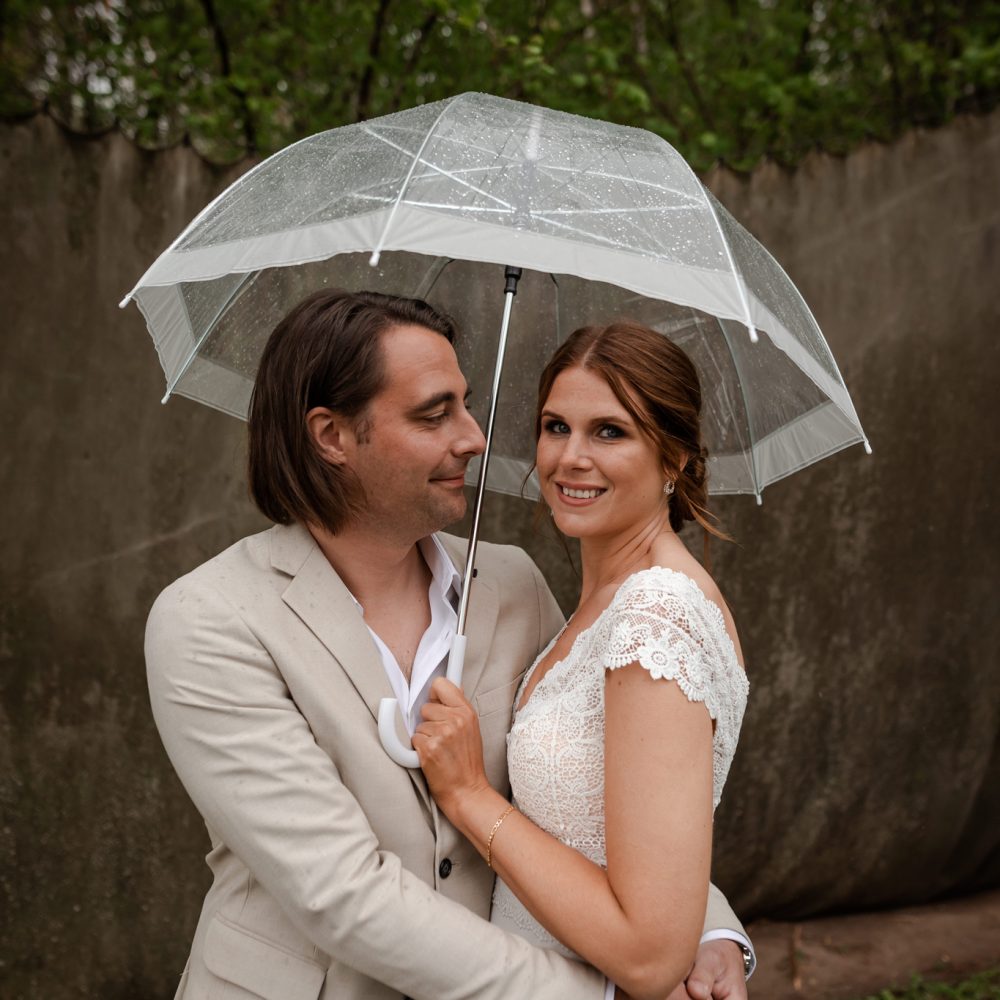 Brudpar poserar under paraply på en regning bröllopsdag