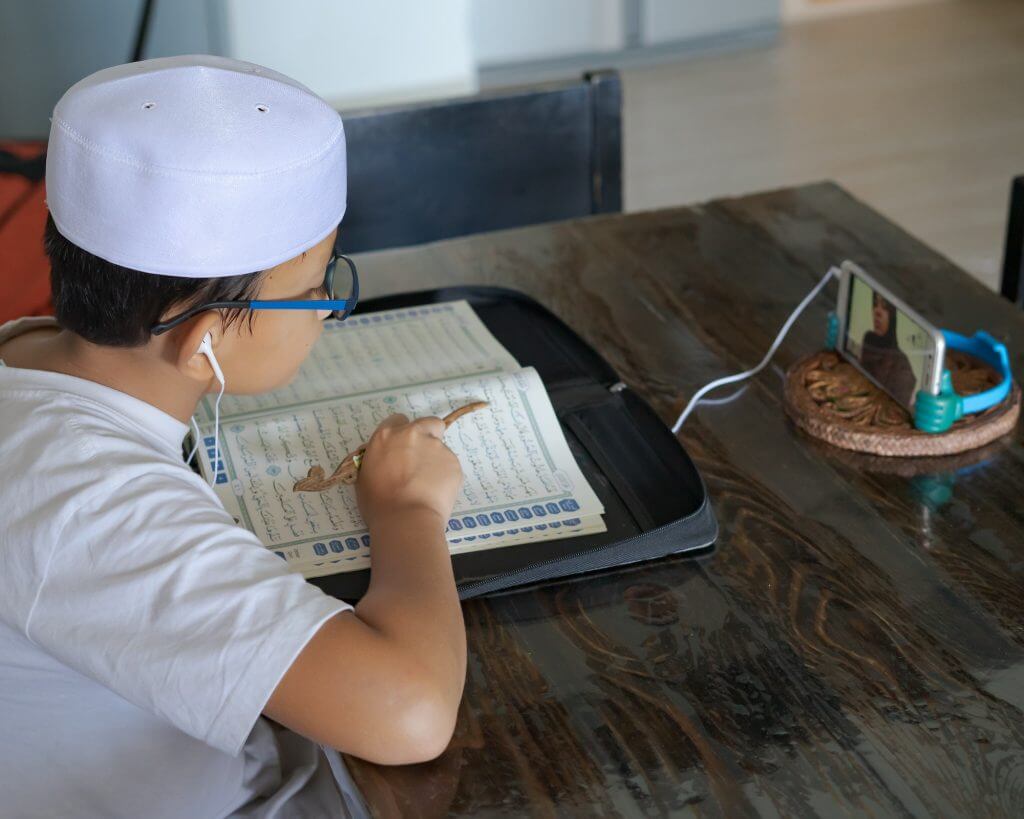 Asian kid reading Al-Quran through video call during education and learning from home for the kid. H