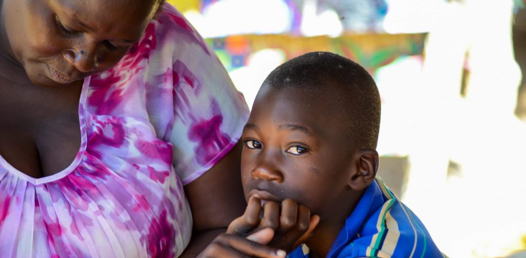 A boy, looking into the camera, sitting with his mother