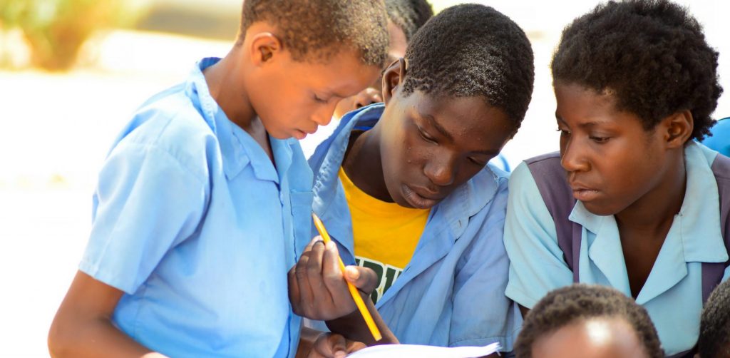 Three school children looking at a piece of paper together.