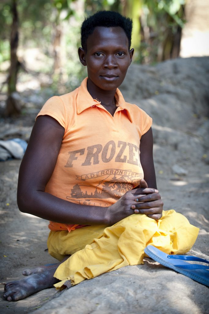 A woman named is sitting on the ground and looks into the camera.