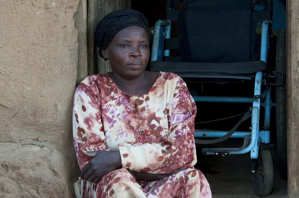 A woman sitting in her doorway, with a wheelchair behind her.