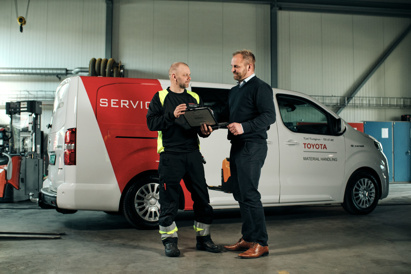 To mænd står foran en servicebil fra Toyota Material Handling og kigger på en skærm, der holdes af den ene person.