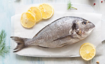 Whole seabream on a board with lemon and herbs.