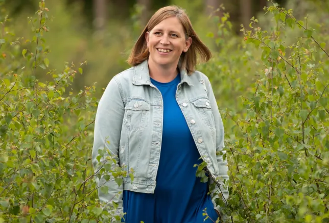 Kirsty in a denim jacket, standing in a field of high grass.