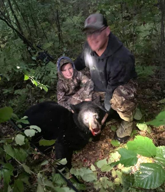 Owen Beierman (L) and father Ryan Beierman (R) crouch next to a dead bear in the woods in 2020 