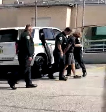 Three sheriff's deputies escort Kieran McKinney out of a patrol car