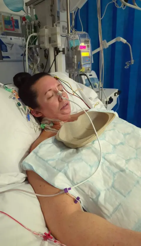 Adele Darlington Adele lying in a hospital bed in intensive care, with her eyes closed, surrounded by tubes
