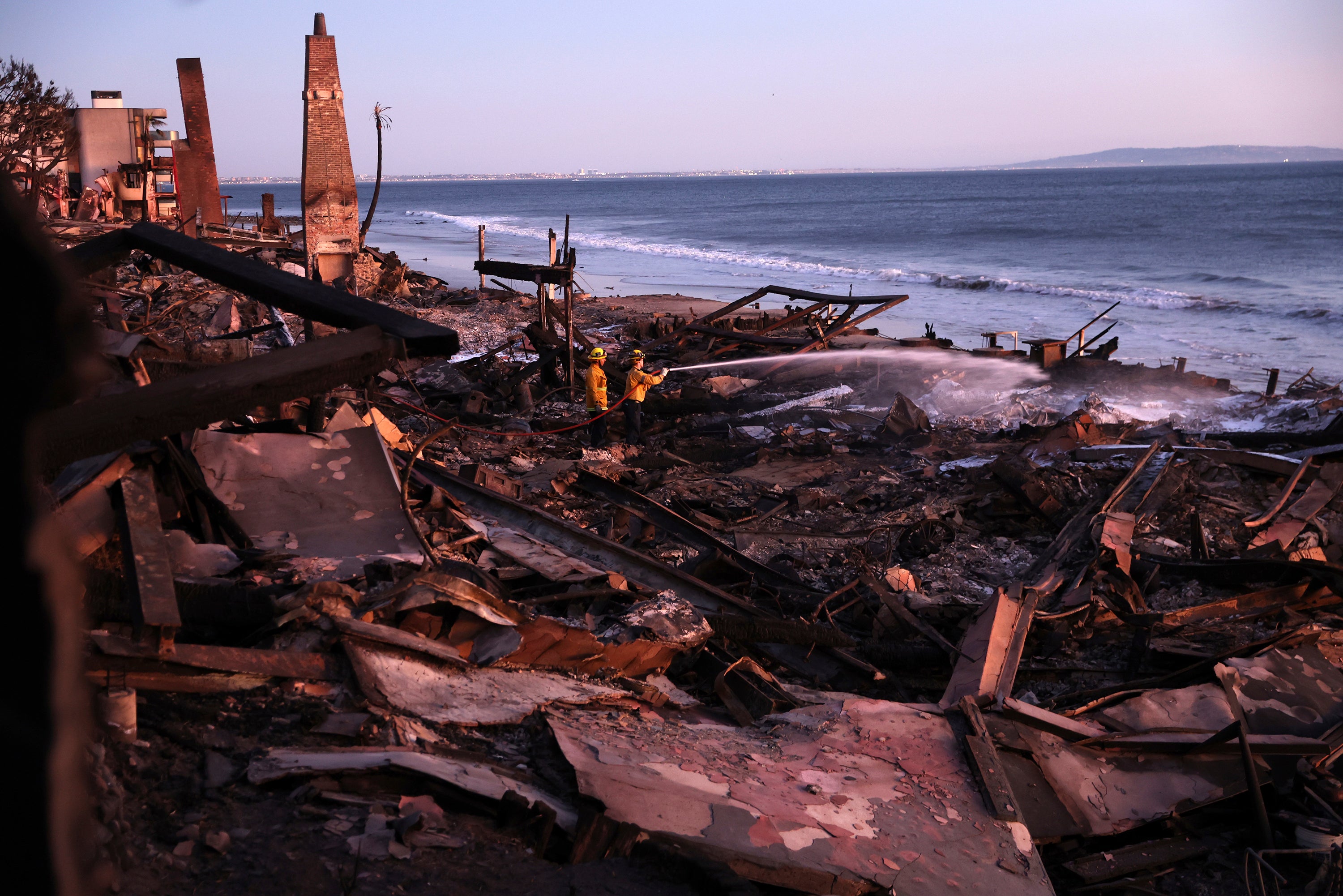 Los Angeles Fire Department’s Dylan Casey and Mike Alvarez work on extinguishing a hot spot along the Pacific Coast Highway in Malibu