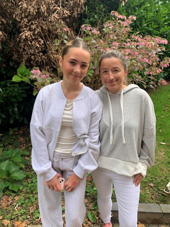 A mother and her teenage daughter stand together outdoors.