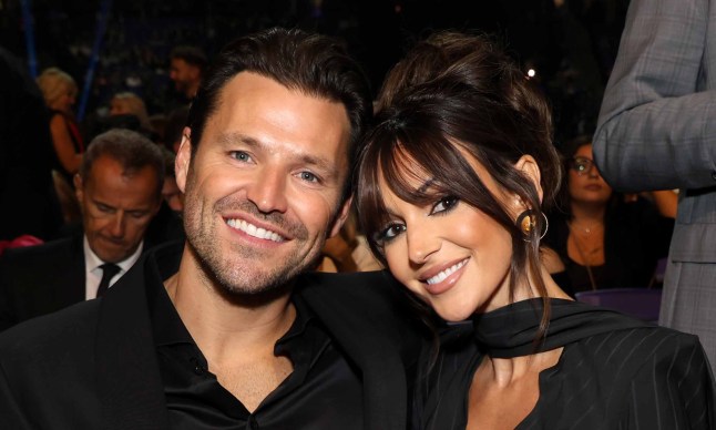 Mark Wright and Michelle Keegan posing together at an event. They are both wearing smart black outfits and smiling