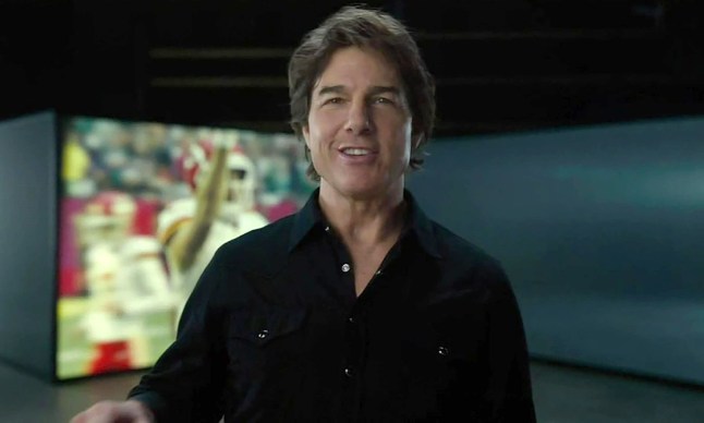 Tom Cruise in the teaser for Mission Impossible 8 standing in front of a screen playing Super Bowl clips